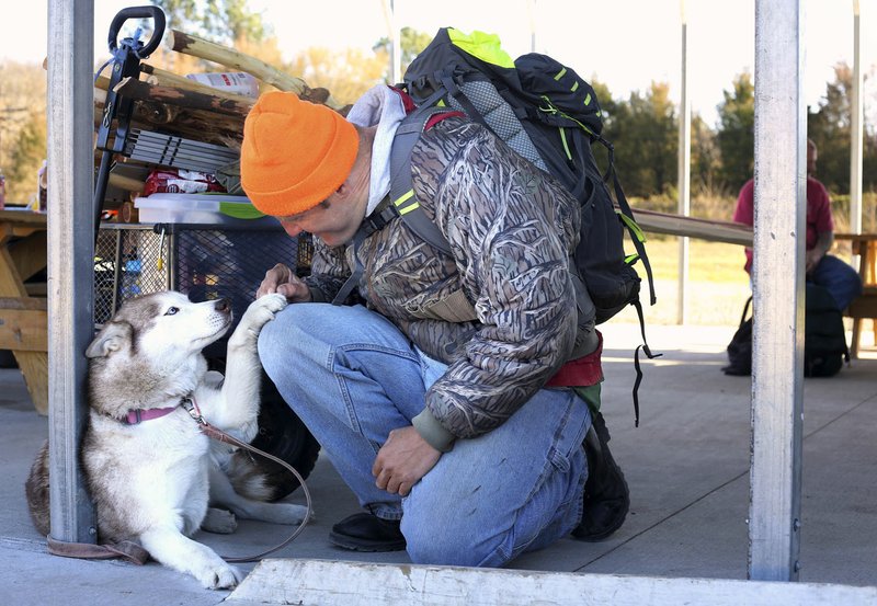 Clarke Mitchell kneels to pet his dog Alice on Feb. 24 next to his wagon filled with wood building material and handmade walking sticks on the covered picnic area at 7 Hills Homeless Center in Fayetteville. Mitchell is one of the skilled laborers that hopes to work at the Homeless Workshop that is in the planning stages.