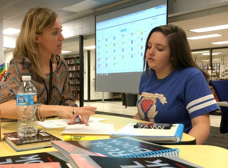 English teacher Cristina Cox (left) gives seventh-grader Savannah Robinson, 13, some tips on writing an essay during Thursday’s meeting of the after-school program the HUB at Lincoln Junior High School in Bentonville. The HUB, which stands for Helping Understand Better, provides students extra help in literacy and math.