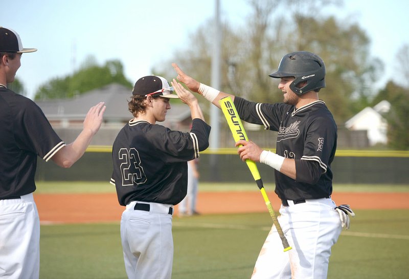 Bentonville High’s Tyler Johnson (right) high-fives teammate Cameron Duncan (23) after scoring in the first inning Monday against Springdale High at the Tiger Athletic Complex in Bentonville.