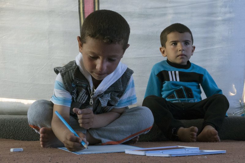 In this Wednesday, April 5, 2017 photo, 6-year-old, Mustafa, left, draws on a piece of paper next to another child in a tent, at the Khazer refugee camp in east Mosul, Iraq, Wednesday, April 5, 2017. 