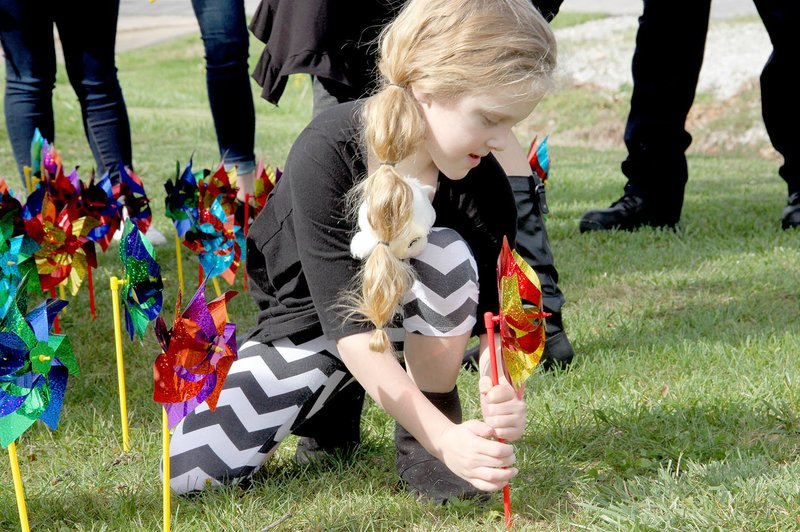 LYNN KUTTER ENTERPRISE-LEADER Bailey Brown, 7, of Lincoln, helps place pinwheels in the ground in front of Prairie Grove City Hall. Each pinwheel represents a child who was abused in Washington County.
