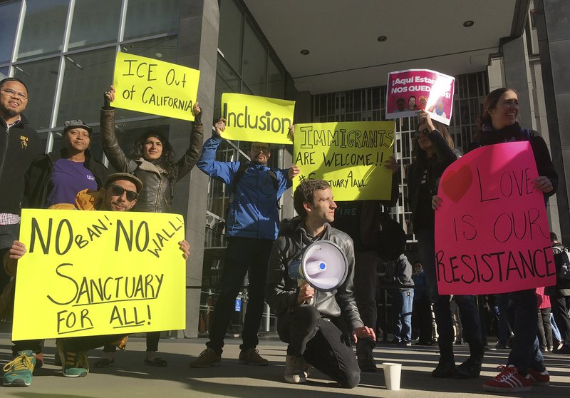 Protesters hold up signs outside a courthouse where a federal judge will hear arguments in the first lawsuit challenging President Donald Trump's executive order to withhold funding from communities that limit cooperation with immigration authorities Friday, April 14, 2017, in San Francisco. 