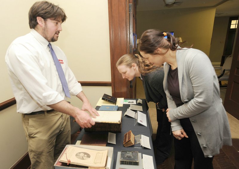 Joshua Youngblood (from left), research and outreach services librarian at University of Arkansas Special Collections, answers questions April 7 at the UA’s Gearhart Hall for Kathleen Lehman and Claire Luchkina, both staff members at the university. The women review a display of some of the historic Bibles the university has in its collection.