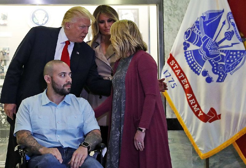 President Donald Trump, left, talks with Tammy Barrientos, right, before awarding a Purple Heart to U.S. Army Sgt. First Class Alvaro Barrientos, as first lady Melania Trump stands second from left, at Walter Reed National Military Medical Center, Saturday, April 22, 2017, in Bethesda, Md.