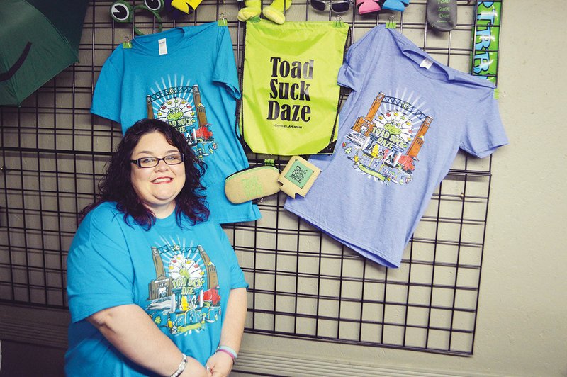 Toad Store employee Tiffany Thornton stands in front of a display of the 2017 festival T-shirts and other items for sale at the store, 1321 Oak St. in downtown Conway. Toad Suck Daze will be May 5-7, but the store will remain open until May 10.