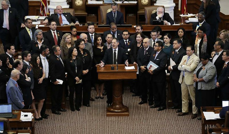 Democratic state Rep. Rafael Anchia, at the lectern surrounded by fellow lawmakers, speaks Wednesday in Austin against a proposed ban on “sanctuary cities” that already has cleared the Texas Senate.