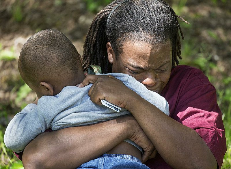 Chris Maxwell clutches his child Thursday afternoon after retrieving him from police at 1805 Park Lane, where his aunt, who operated the day care, died in a drive-by shooting. Police said the 60-year-old woman was killed by a stray shot when a neighboring house was targeted. No children were hurt. More photos are available at arkansasonline.com/galleries.