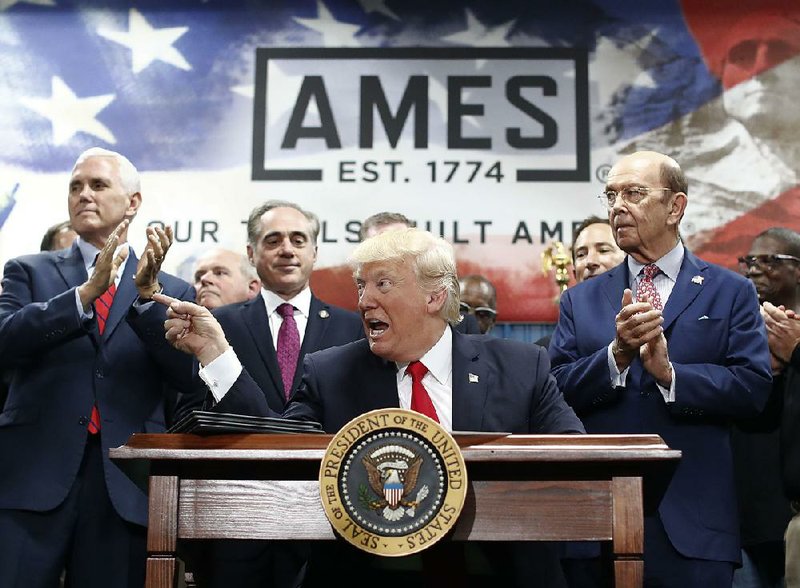 President Donald Trump — flanked Saturday in Harrisburg, Pa., by Vice President Mike Pence (rear, from left), Secretary of Veterans Affairs David Shulkin and Secretary of Commerce Wilbur Ross — signs an executive order to establish an office of trade and manufacturing policy at the White House.