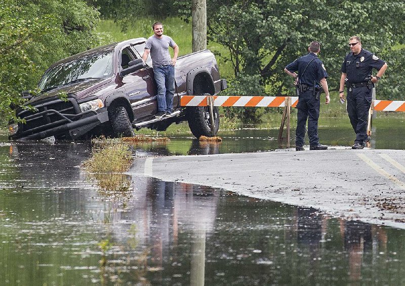 Sherwood police wait for help from Gravel Ridge fi refi ghters Sunday after a driver got stuck in high water while trying to go around a barricade blocking Jacksonville-Cato Road.