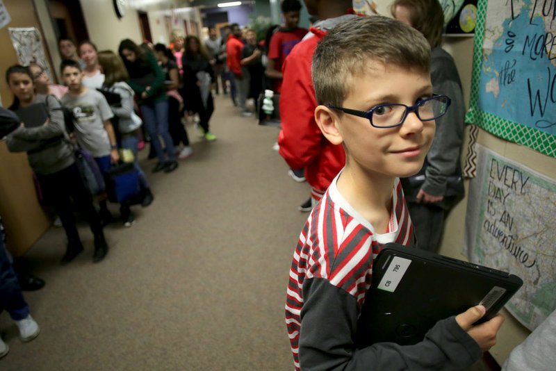 Aiden Thomas, a sixth-grade student at Holt Middle School, clutches his Chromebook on Wednesday in the hallway as he stands with students before transferring to his next class.