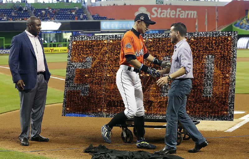 Miami outfielder Ichiro Suzuki shakes hands with club president David Samson in front of a photo collage honoring Ichiro’s 3,000th hit.