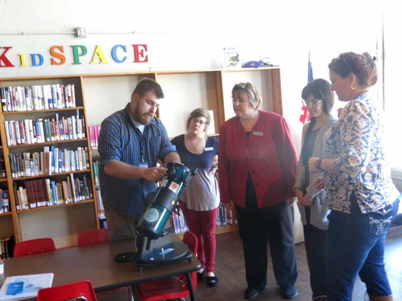 Photo by Susan Holland Van Masterson (left), of Rogers, came to Gravette last week and showed staff members at Gravette Public Library how to use the new Orion StarBlast reflecting telescope they would soon receive for checkout. Here Masterson explained the features of the telescope to library aide Brittany Shreve, library supervisor Karen Benson and library aide Artemis Edmisten while Katherine Auld (right), president of the Sugar Creek Astronomical Society, looked on.