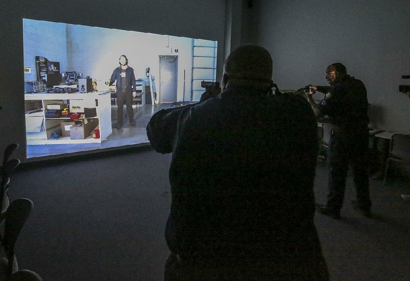 Little Rock police officers Herb Kimbrough (left) and Ira Whitfield demonstrate a use-of-force training simulator Thursday at the Police Department’s training facility.