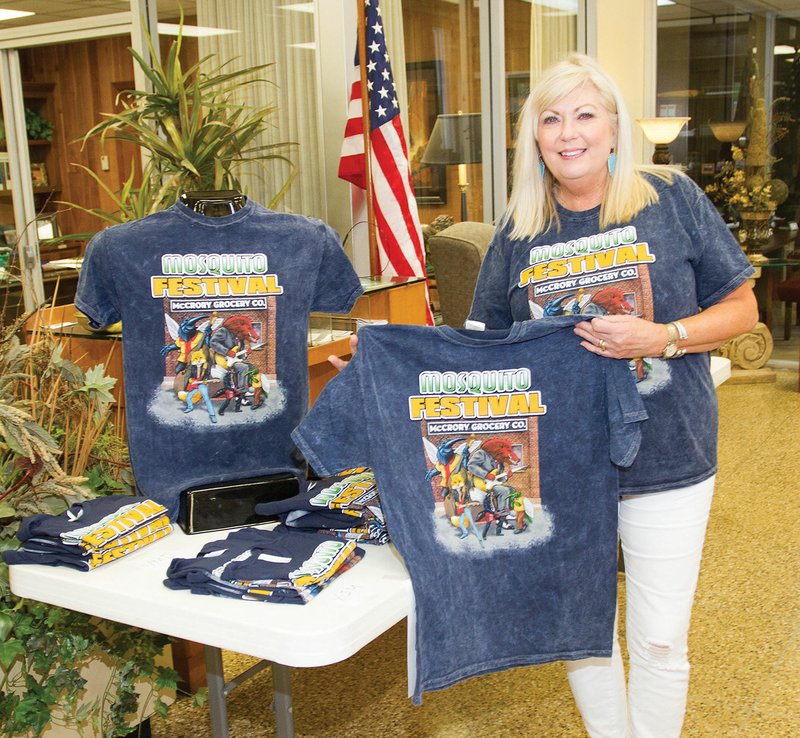 Betty Kate Thompson, president of the McCrory Chamber of Commerce, stands with a T-shirt display for the 32nd annual Mosquitofest at the Bank of McCrory. The festival will be May 18-20.