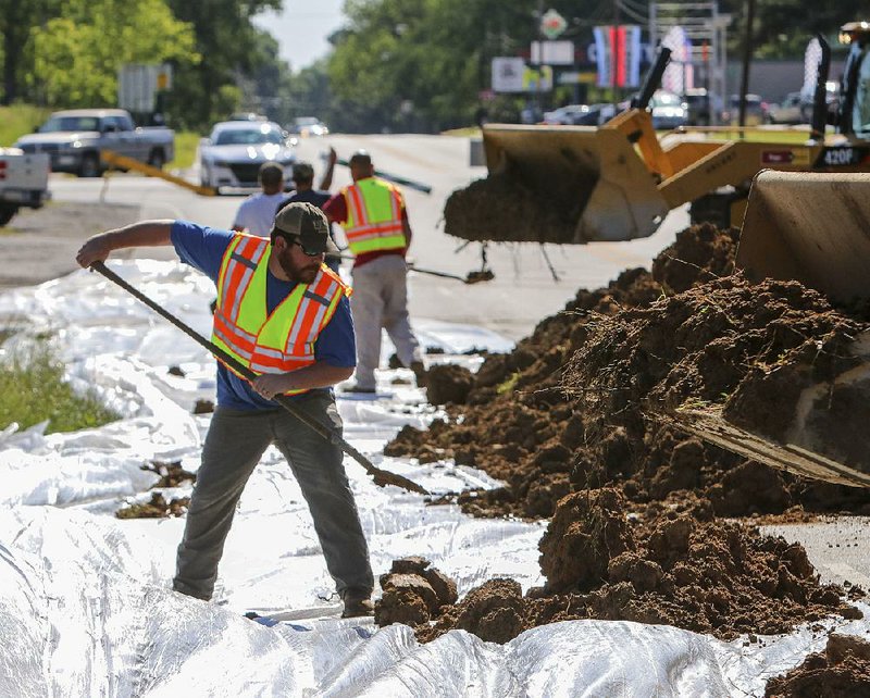 City workers and volunteers build a 5-foot-tall dirt wall Friday morning along Main Street in downtown Des Arc in anticipation of rising water. During a 2011 flood, residents built the same type of wall in the same location to protect homes on the south side of Main Street.