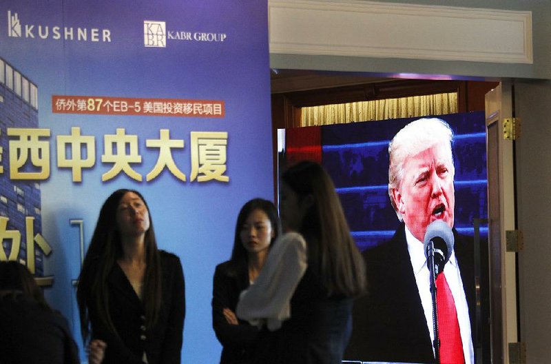 A projector screen shows footage of U.S. President Donald Trump as workers wait at a hotel in Shanghai, China, on Sunday to talk with potential investors during an event promoting investment in a Kushner Companies development. 