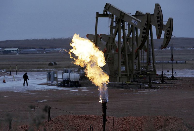 Workers tend to pump jacks operating near a natural gas flare outside Watford City, N.D., in this file photo. Gas flaring is so prevalent in North Dakota that nighttime flaring at drilling sites is visible from space.