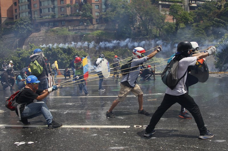 Anti-government protesters work together to aim a giant slingshot holding a glass bottle of fecal matter, at security forces blocking their march from reaching the Supreme Court in Caracas, Venezuela, Wednesday, May 10, 2017. 