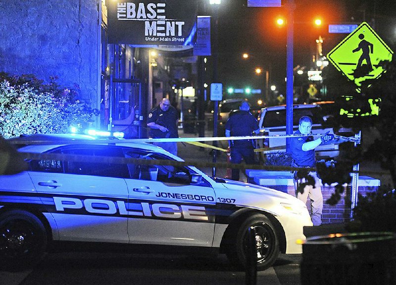 An officer lifts crime scene tape Sunday morning to let a police cruiser through at the scene of a fatal shooting in downtown Jonesboro. One person was killed and six others were injured.