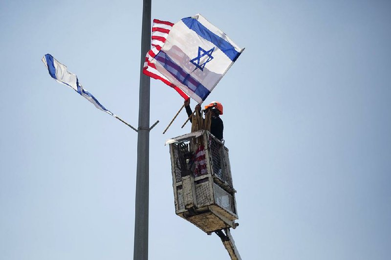 A worker hangs U.S. and Israeli !ags on a lamppost on a freeway leading to Jerusalem on Tuesday in preparation for President Donald Trump’s visit next week.