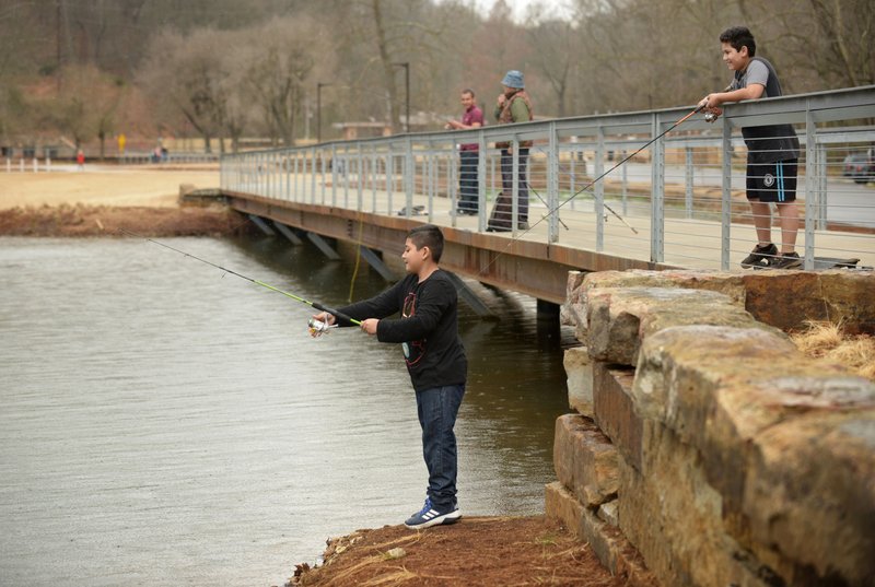 NWA Democrat-Gazette/File Photo Two boys cast lines while fishing at Lake Atalanta in Rogers. The city is considering changes to the park's hours.