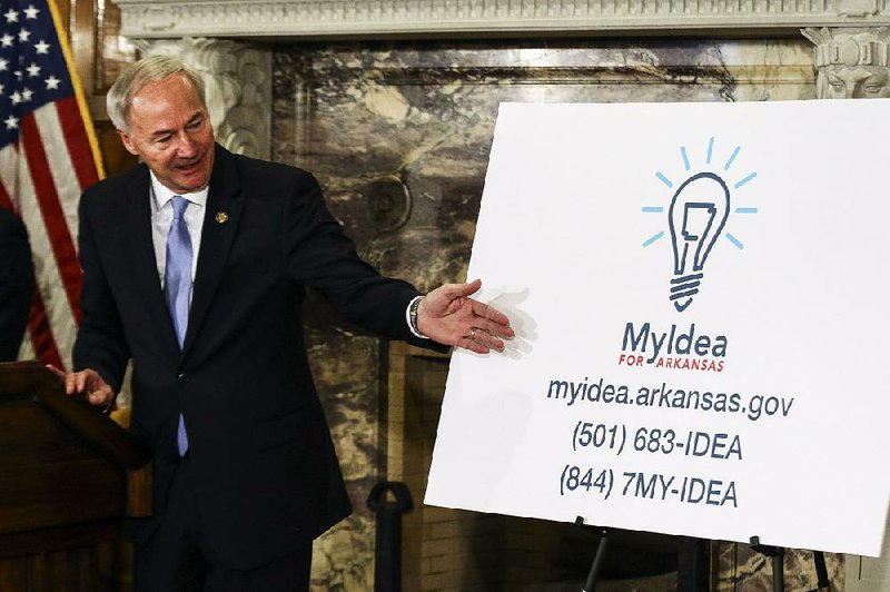 Gov. Asa Hutchinson shows the new logo and contact information for the MyIdea project at the state Capitol on Thursday. People, by telephone or website, can make suggestions for state government improvements. 