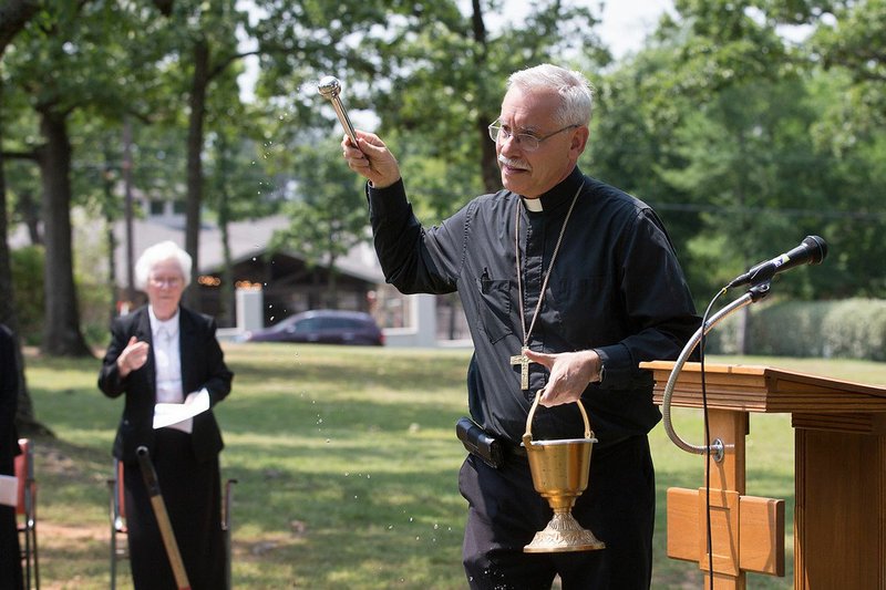Special to the Democrat-Gazette/KAREN SCHWARTZ Waving an aspergillum, Bishop Anthony Taylor blesses the grounds of St. Scholastica during the ground-breaking celebration.
