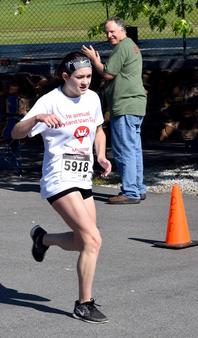 Photo by Mike Eckels With Bob Bland (background) cheering her on, Rebekah Wendt crossed the finish line of the Gayland Van Dyke Memorial 5K Run at Veterans Park in Decatur May 13. Wendt, the granddaughter of Van Dyke, was the overall winner of the event with a time of 22:30.