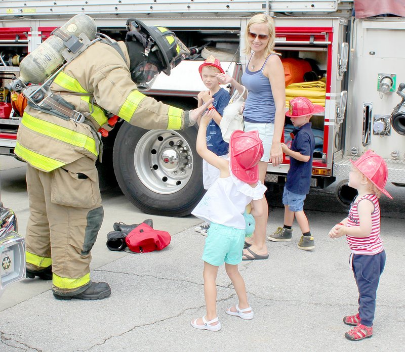 Keith Bryant/The Weekly Vista Firefighter-paramedic Brian Mowery, left, high-fives Coralyn Gore, 3, while her brother, Grayelen Gore, 9; mother, Hilary Gore; and brother Lochlan Gore, 5, stand back. Ezra Luka, 2, stands back and watches.