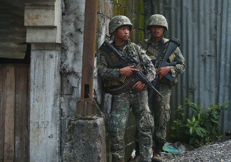 Philippine marines pause behind a wall Sunday as they move through the contested city of Marawi. Forces are battling to recapture the city from militants linked to the Islamic State.  