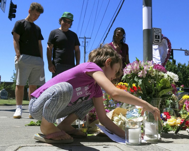 Coco Douglas, 8, leaves a handmade sign and rocks she painted at a memorial in Portland, Ore., on Saturday, May 27, 2017, for two bystanders who were stabbed to death Friday while trying to stop a man who was yelling anti-Muslim slurs and acting aggressively toward two young women. From left are Coco's brother, Desmond Douglas; her father, Christopher Douglas; and her stepmother, Angel Sauls. 