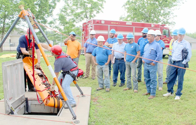 Keith Bryant/The weekly Vista Firefighter-EMT Ryan Carr, left, helps to heft a safely-restrained mannequin from a maintenance access hatch with help from firefighter-paramedic Josh Whitaker while water department workers observe.