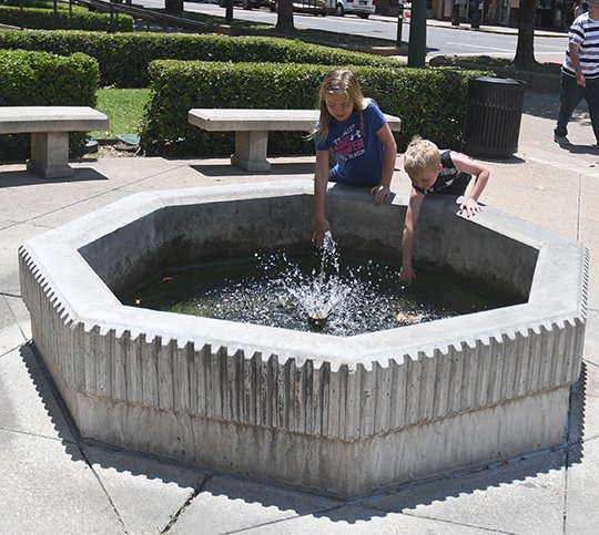 The Sentinel-Record/Mara Kuhn HASHTAG HSNP: Marissa Tusler, 9, and Bennett Tusler, 6, of Minneapolis, test Hot Springs National Park’s namesake hot water in the thermal display fountain outside the Fordyce Bath House on Monday.