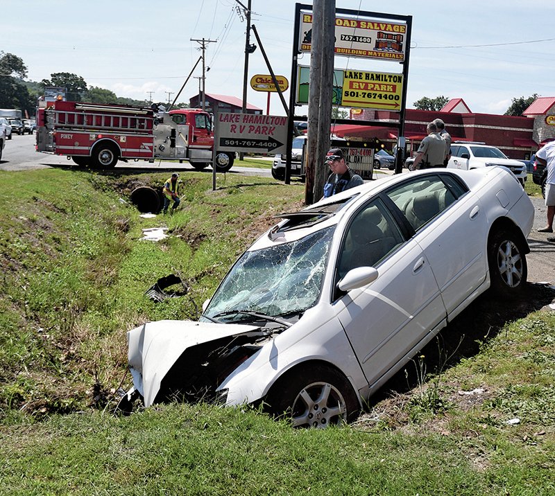 The Sentinel-Record/Mara Kuhn Emergency personnel work the scene of a one-vehicle wreck in the 3000 block of Albert Pike Road Wednesday morning. The male driver of a Nissan Altima was westbound at a high rate of speed when he crossed several lanes of traffic and crashed in the ditch on the east side of the roadway, Arkansas State Police Cpl. Michael Reed said. Piney Fire Department personnel deployed containment booms in the ditch to prevent the spread of leaking oil. The female passenger was injured and transported by LifeNet to a local hospital and the driver was cited for careless driving.
