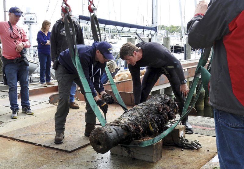 In this May 24, 2017 photograph provided by the U.S. Navy, Naval History and Heritage Command underwater archaeologist George Schwarz, right, and Explosive Ordnance Disposal Technician Senior Chief Mark Faloon, left, stand over and prepare a cannon for transportation at Dodson Boat Yard in Stonington, Conn. to the Washington Navy Yard. The cannon is believed to be from the wreck of U.S.S. Revenge in 1811.