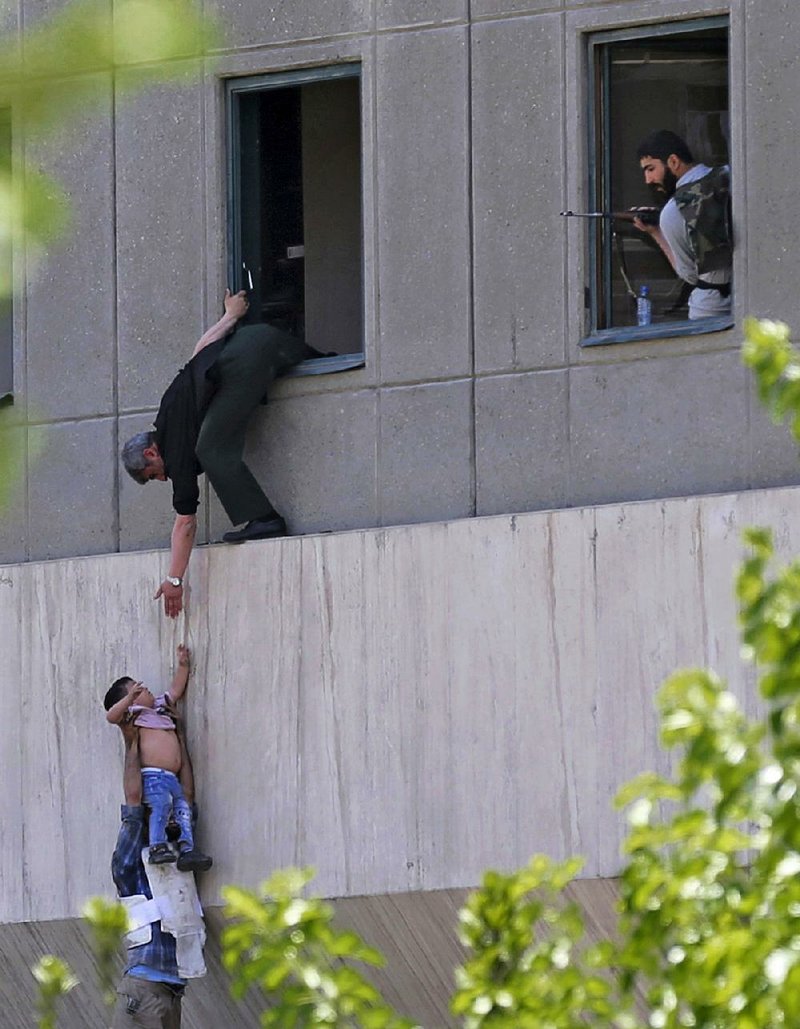 A man hands a child down to a security guard Wednesday at Iran’s parliament building in Tehran after suicide bombers and gunmen stormed that building and the tomb of Ayatollah Ruhollah Khomeini.