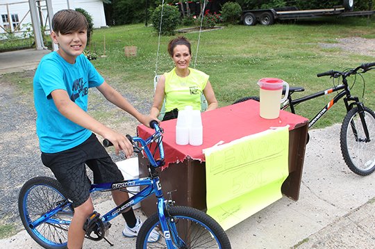 The Sentinel-Record/Richard Rasmussen HAPPY ENDING: Kaleb Hayes, 14, is all smiles on top of his new bicycle Monday as he and his mother, Nicole Hayes, man his lemonade stand outside his home on Woodlawn Avenue. Hayes was raising money to buy a bicycle and a Facebook post on Thursday prompted an outpouring of support from the community, with two bicycles being given to him.