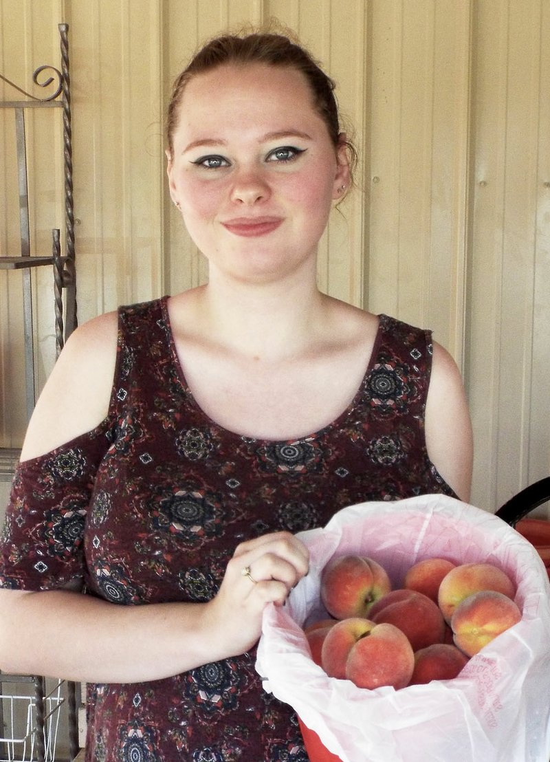 Photo by Randy Moll Carol Williams, 19, shows a bucket of peaches at Taylor&#8217;s Orchard on Friday. The orchard opened Friday morning and will continue to offer peaches, nectarines and blackberries over most of the summer months. Orchard hours are 8 a.m. to 6 p.m., Monday through Saturday.