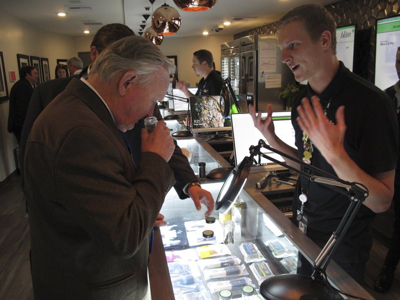 FILE- In this March 24, 2017 file photo, Nevada state Sen. Don Gustavson, R-Sparks, smells a sample of marijuana as Christopher Price, a ''budtender'' at the Blum medical marijuana dispensary, describes the operation during a brief tour a the store in Reno, Nev. A judge in Nevada is trying to decide whether the state's first sales of recreational marijuana should begin as scheduled July 1 despite complaints from alcohol distributors. (AP Photo/Scott Sonner, File)