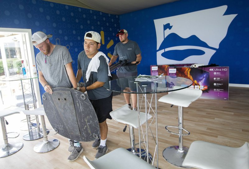 Austin Comiskey (from left), Mike Vasquez and Drew Clark, all with Roark Group, set up a television stand Wednesday in the seating area overlooking the 18th green at Pinnacle Country Club in Rogers. Events begin Monday for the LPGA Walmart NW Arkansas Championship.
