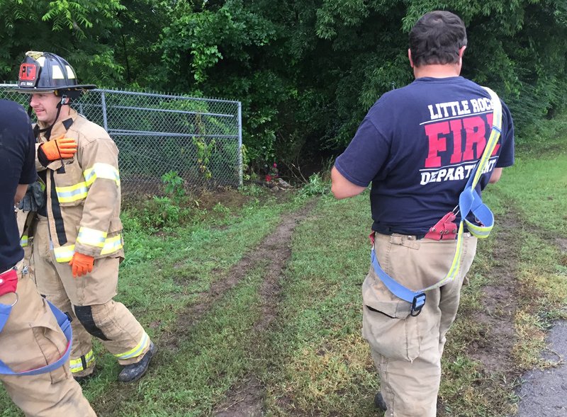 Little Rock Fire Department officials stand at the scene of an accident where a car ran off a roadway and into a creek Monday morning.