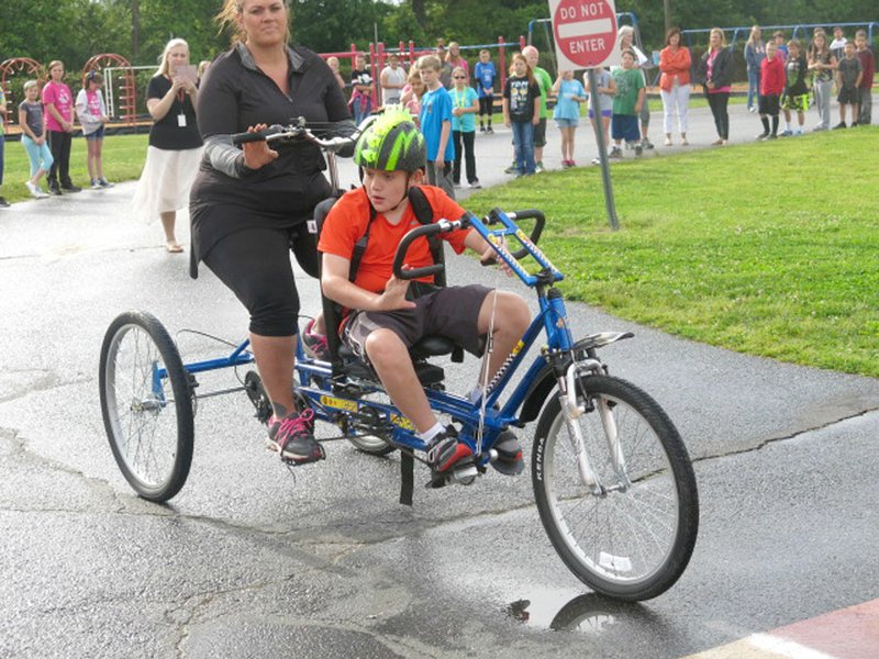 Photo by Susan Holland Brock Beccard, riding the specially-equipped bicycle purchased for him with schoolmates&#8217; donations, rounds a turn on the track on the Gravette Upper Elementary School playground. Brock, with his mother Michaela riding behind, made a full lap of the track as his fellow students cheered him on.