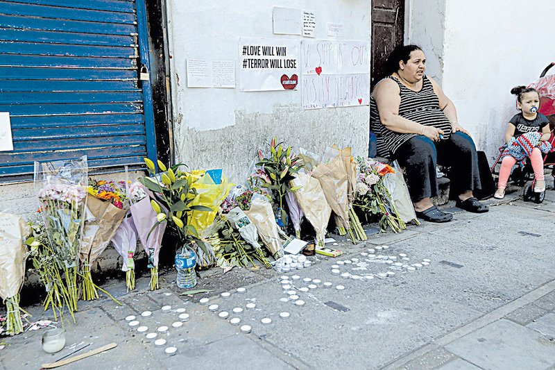 A woman and child sit Tuesday next to floral tributes placed at the scene of an attack near a mosque in the Finsbury Park area of north London. 