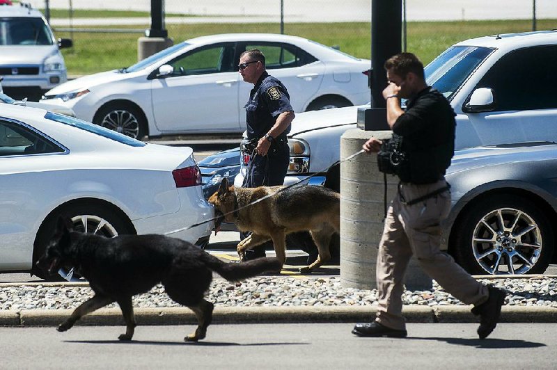 Police dogs search cars in a parking lot at Bishop International Airport on Wednesday in Flint, Mich.