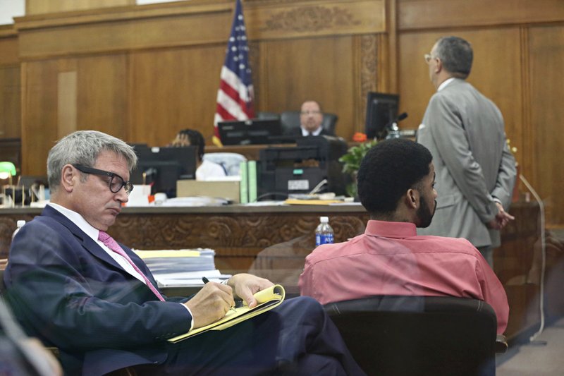 Dominique Heaggan-Brown, right, and his attorney Jonathan C. Smith, left, watch the power point presentation of use of force expert, Robert C. Willis on a video screen during the trial of former Milwaukee officer Heaggan-Brown Monday, June 19, 2017, in Milwaukee. A police expert in the use of deadly force says on Monday that Heaggan-Brown, on trial for fatally shooting a black man after a foot chase "acted in accordance with his training." Attorney Steven R. Kohn is at upper right. (Michael Sears/Milwaukee Journal-Sentinel via AP, Pool)