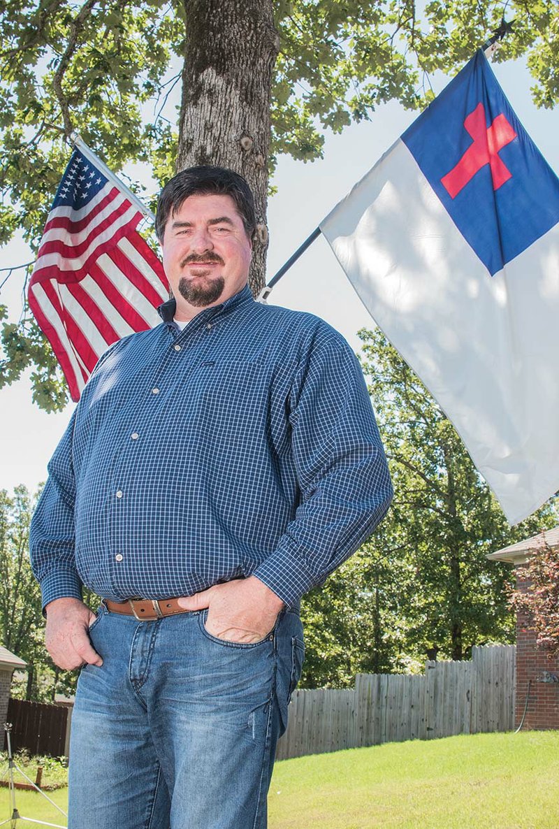 Eddy York, new president of the Mayflower Chamber of Commerce, stands underneath the American and Christian flags at his home. York, who is also a member of the City Council, said he rededicated his life to Jesus Christ three years ago, and it has changed how he deals with people. York said his sixth-grade teacher, Lloyd Hervey of Conway, encourages him on his spiritual path, as well as David Fox, pastor of First Baptist Church.