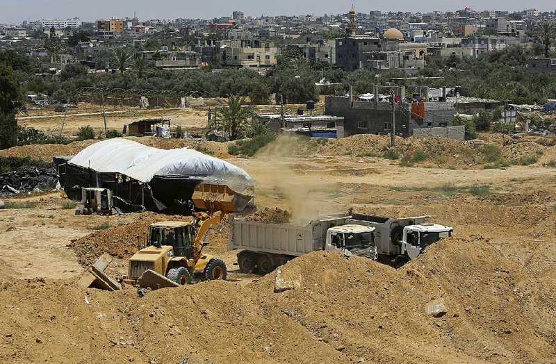 A backhoe removes sand hills to create a buffer zone along the Egyptian border with the Gaza Strip near smuggling tunnels (center left) Wednesday in Rafah.