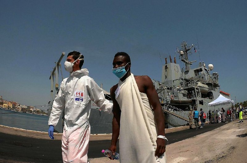 An Italian paramedic escorts a migrant Friday during the disembarkment of 402 migrants from a British navy ship in the harbor of Brindisi, Italy. 