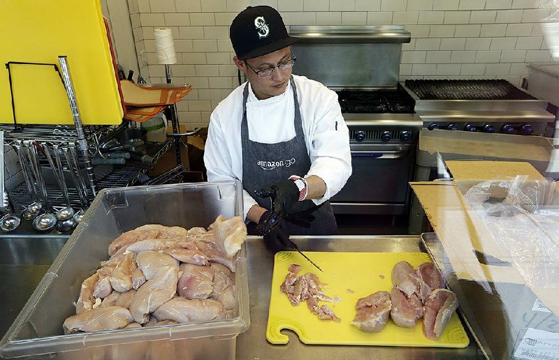 A worker at a Seattle Amazon Go store, currently open only to Amazon employees, is seen through an exterior window as he cuts up chicken earlier this year.