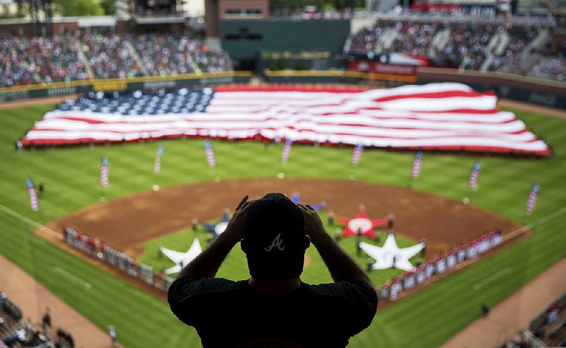 A spectator takes a photo of a United States flag during the national anthem at a recent Major League Baseball game between Atlanta and Washington. The anthem has been a part of U.S. sports games since World War II, with some experts agreeing that Game 1 of the 1918 World Series between the Boston Red Sox and the Chicago Cubs helped pave the way.